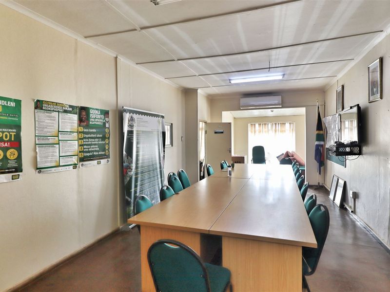 A functional office space featuring a long boardroom table, split-system air conditioning, and standard office lighting, suitable for meetings or collaborative work.