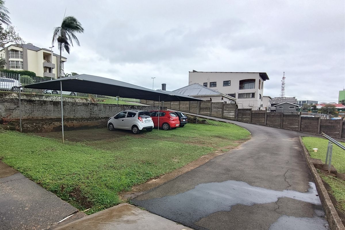 Outdoor parking area featuring a shade cloth carport structure, asphalt driveway, and perimeter retaining walls.
