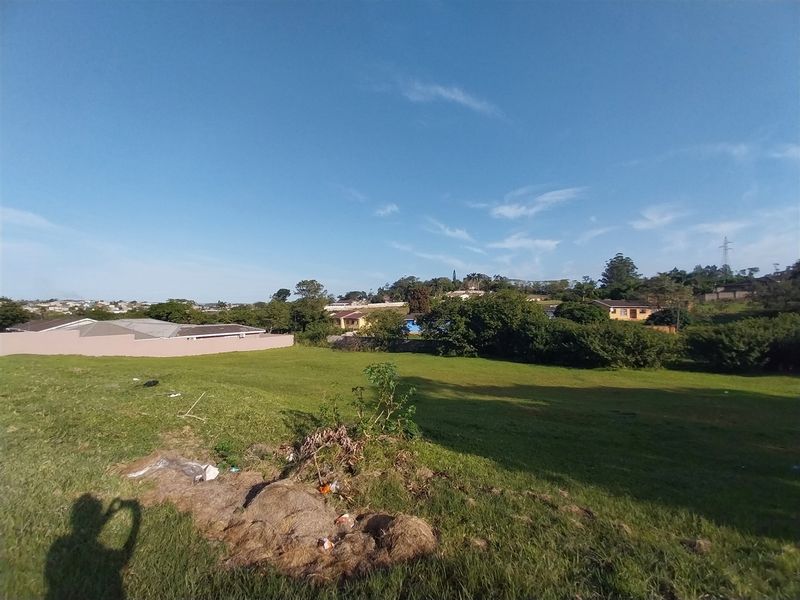 A view of a vacant residential plot featuring a grass lawn and surrounding perimeter wall in a suburban neighborhood.