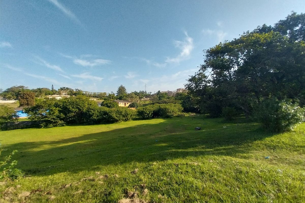 A spacious, gently sloping residential plot featuring established trees and a well-maintained grass lawn in a quiet neighborhood setting.