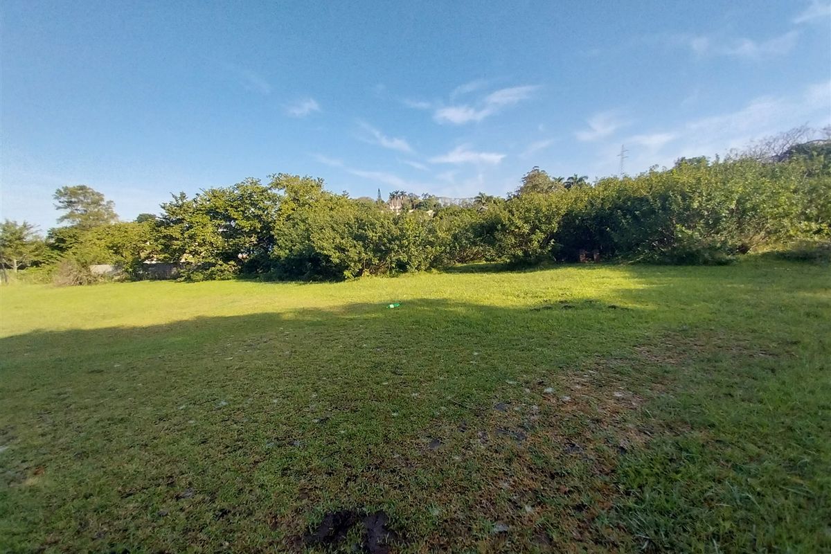 A spacious, level residential plot featuring a well-maintained grass lawn and established perimeter trees, offering a private setting for future development.