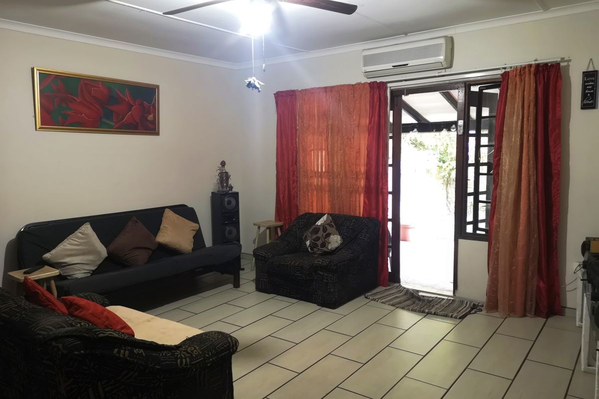 A living room featuring tiled flooring, a ceiling fan, and a wall-mounted air conditioning unit, with direct access to an outdoor patio area.