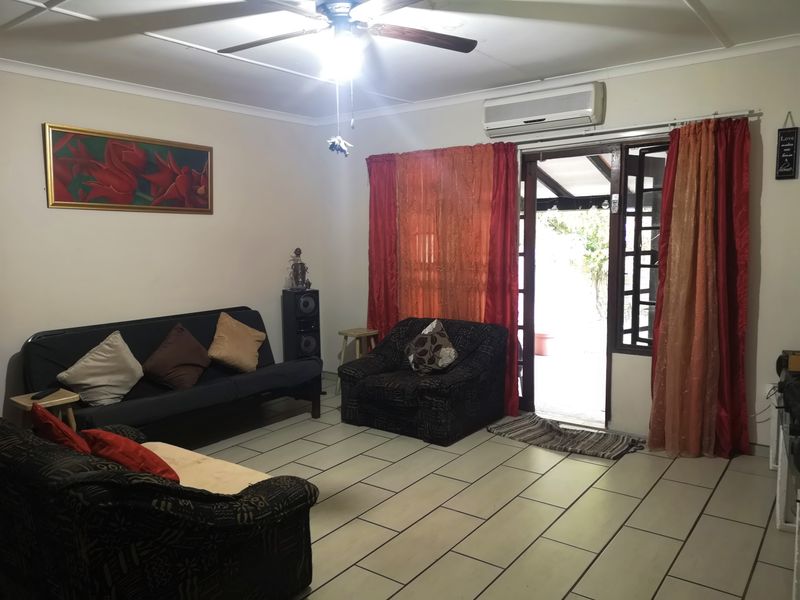 A living room featuring tiled flooring, a ceiling fan, and a wall-mounted air conditioning unit, with direct access to an outdoor patio area.