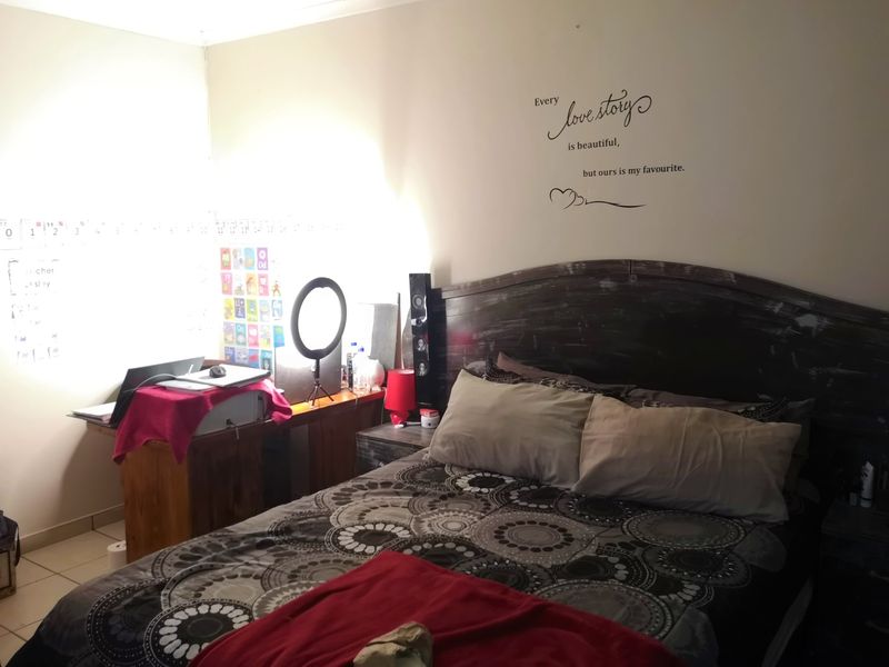 A standard bedroom featuring neutral wall finishes and tiled flooring, currently utilized as a combined sleeping and workspace area.