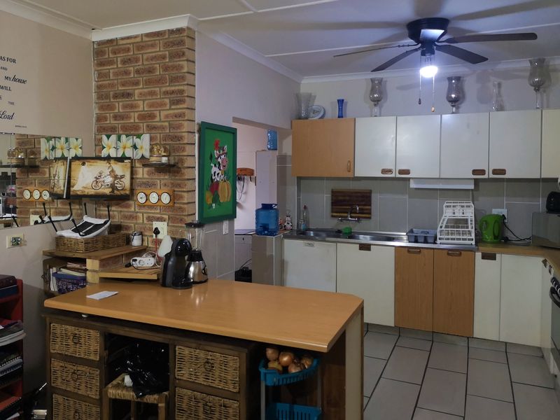 A functional kitchen featuring an exposed brick wall, tiled flooring, and a mix of wood-tone and white cabinetry with a central island workspace.