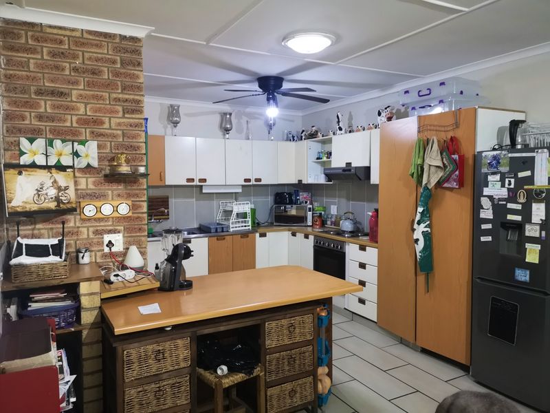 A functional kitchen featuring exposed brickwork, white and wood-tone cabinetry, built-in oven with extractor, and tiled flooring.