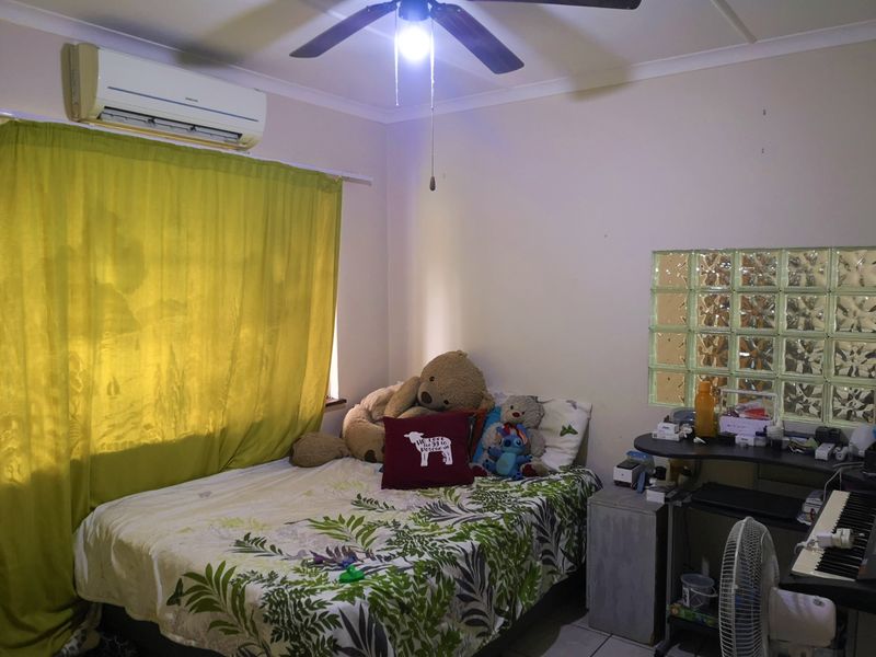 A bedroom featuring a ceiling fan, wall-mounted split-system air conditioner, and a decorative glass block feature wall.