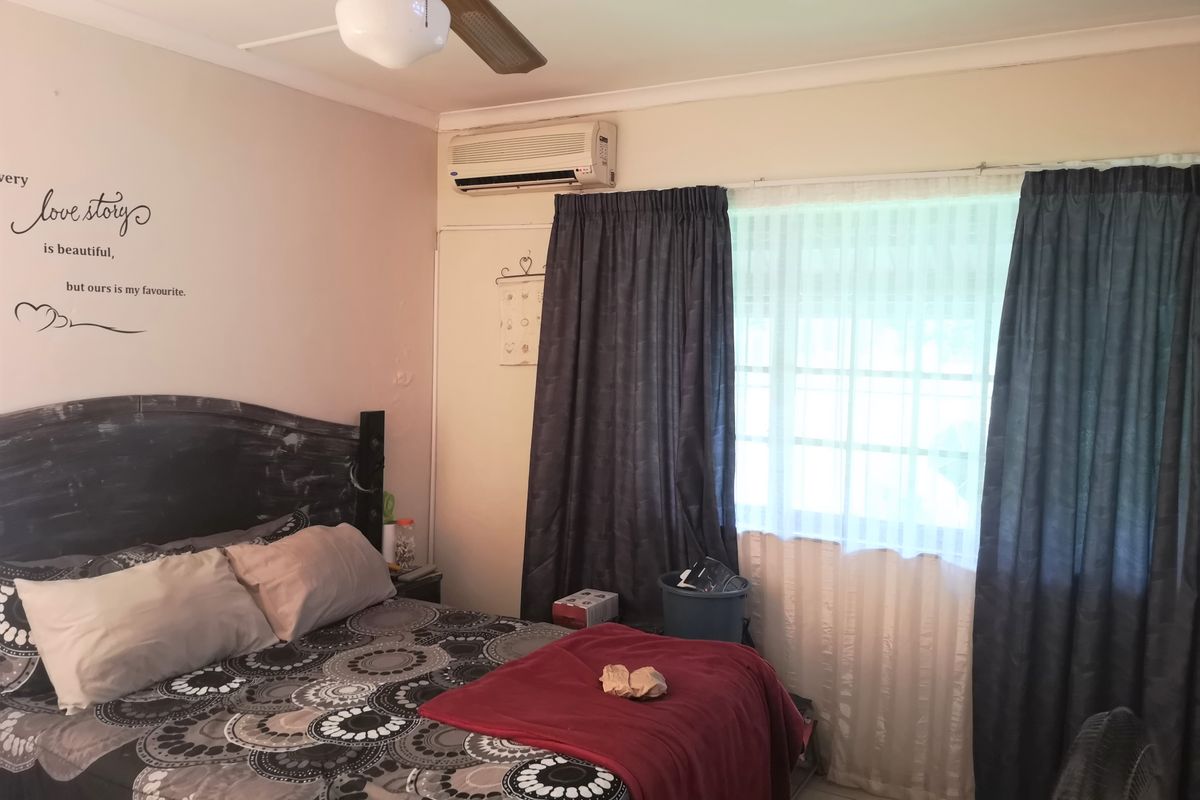 A functional bedroom featuring tiled flooring, a ceiling fan, and a wall-mounted split-system air conditioning unit.