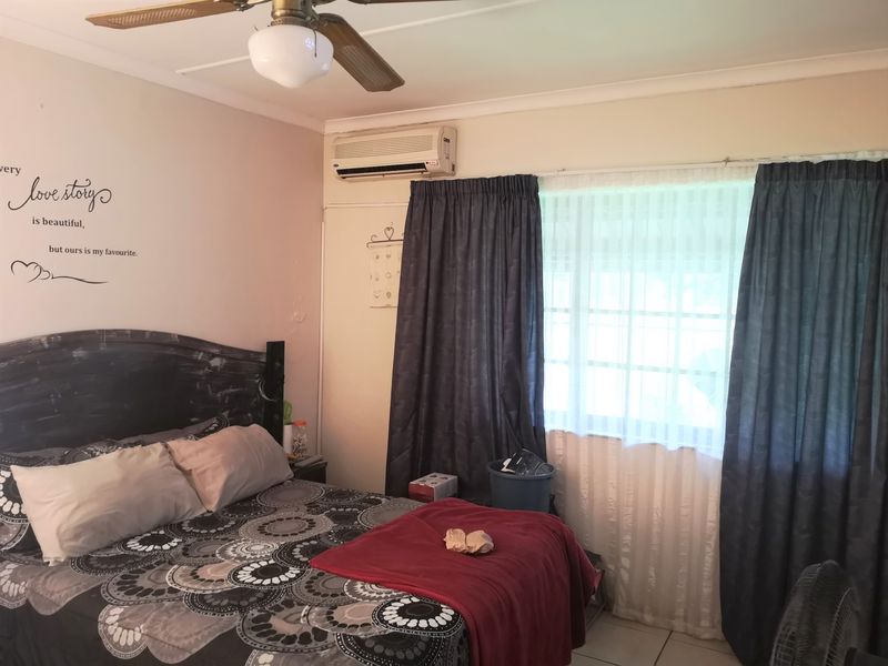A functional bedroom featuring tiled flooring, a ceiling fan, and a wall-mounted split-system air conditioning unit.