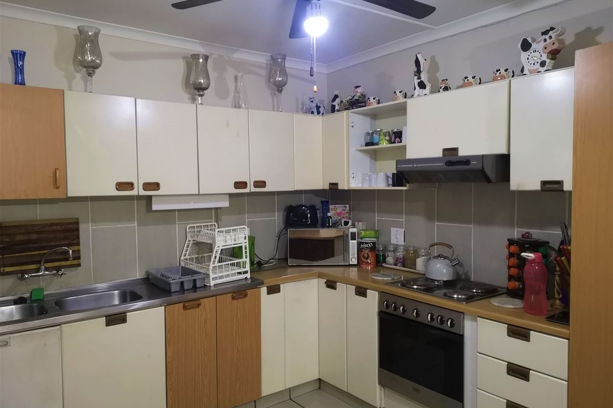A functional kitchen featuring built-in cabinetry, a stainless steel sink, an electric oven with hob, and an extractor fan with tiled backsplash.