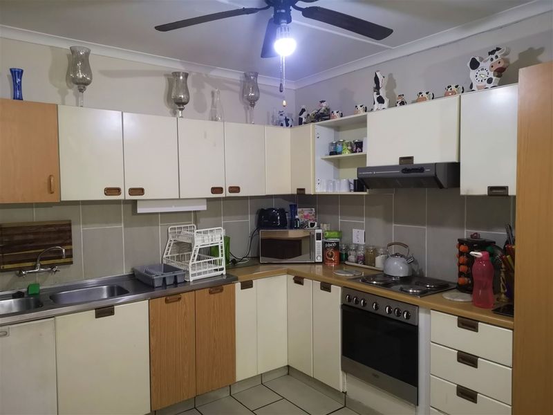 A functional kitchen featuring built-in cabinetry, a stainless steel sink, an electric oven with hob, and an extractor fan with tiled backsplash.