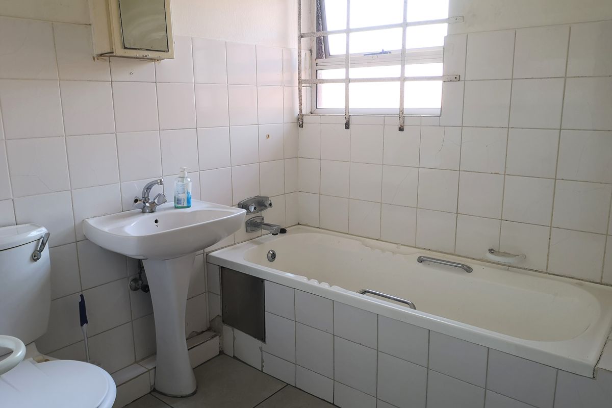 A dated bathroom featuring a pedestal basin, bathtub with chrome fixtures, and white wall tiling. The space requires cosmetic updates to modernize the finishes.