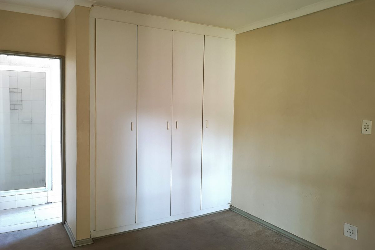 A vacant bedroom featuring built-in cupboards, neutral wall finishes, and carpeted flooring, with an adjacent doorway leading to a tiled area.