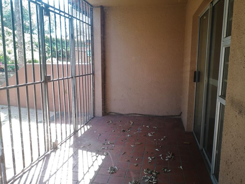 A covered patio area featuring tiled flooring, a security gate, and a sliding glass door providing access to the interior.