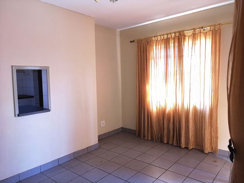 An empty living area featuring tiled flooring and a convenient serving hatch connecting to the kitchen, providing a functional blank canvas for renovation.