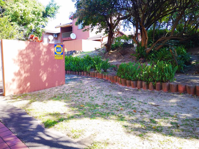 Front exterior view of the townhouse property featuring a boundary wall, security signage, and established garden area with a paved walkway.