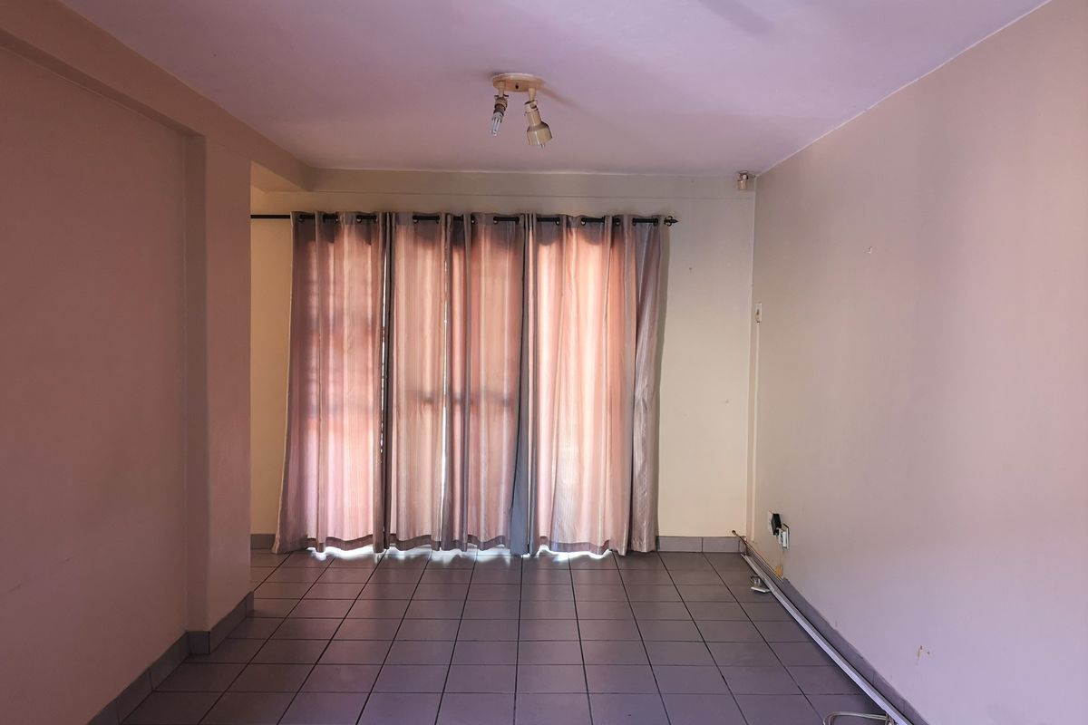 An empty living room featuring tiled flooring, neutral walls, and a large window with curtain rod, ready for personalization.