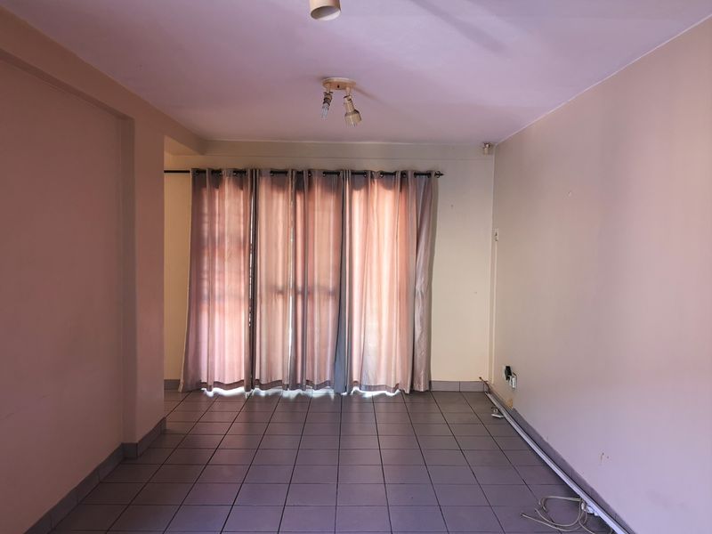 An empty living room featuring tiled flooring, neutral walls, and a large window with curtain rod, ready for personalization.