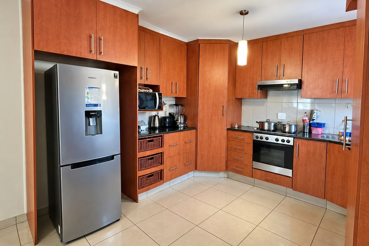 A functional kitchen featuring warm-toned wooden cabinetry, granite countertops, built-in oven with extractor fan, and neutral tiled flooring.