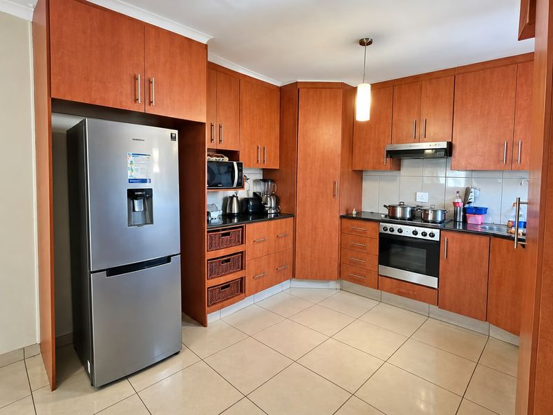A functional kitchen featuring warm-toned wooden cabinetry, granite countertops, built-in oven with extractor fan, and neutral tiled flooring.