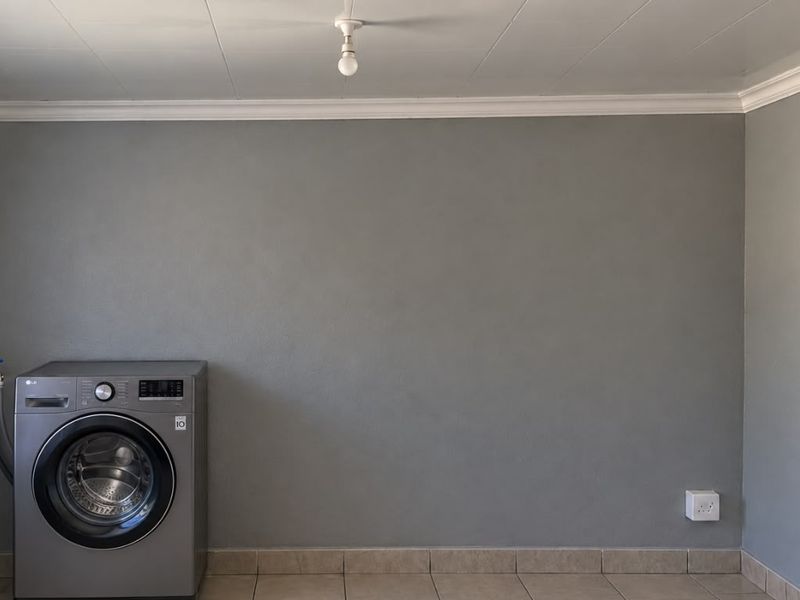 A functional laundry room featuring tiled flooring, a dedicated plumbing connection for a washing machine, and a window with security bars.