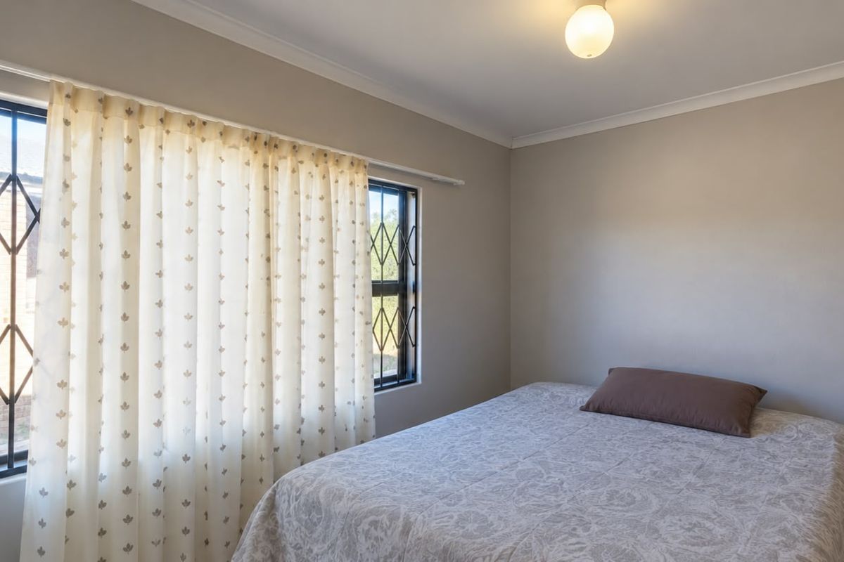 A simple bedroom featuring neutral wall tones, security bars on the windows, and functional curtain rails.