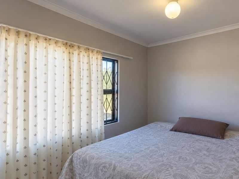 A simple bedroom featuring neutral wall tones, security bars on the windows, and functional curtain rails.
