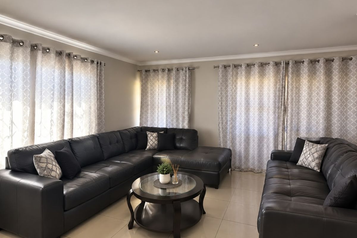 A well-maintained living room featuring neutral tiled flooring, recessed downlighting, and decorative curtain rails, creating a comfortable and bright living space.