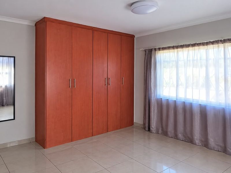 A bright, empty bedroom featuring neutral tiled flooring and ample built-in wooden cupboards, providing a clean and versatile space.