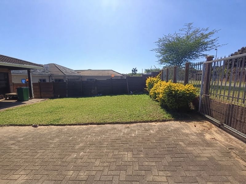 A private rear garden area featuring a paved driveway, a well-maintained lawn, timber boundary fencing, and a secure metal gate.