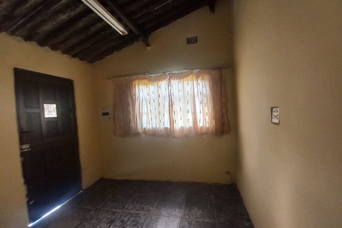 A simple, empty bedroom featuring tiled flooring, a single window with curtains, and an exposed rafter ceiling.