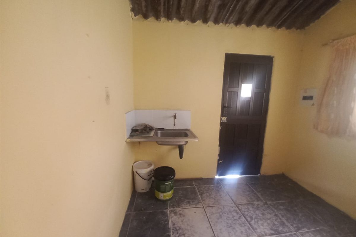 A basic utility or kitchen area featuring a wall-mounted sink, tiled flooring, and direct exterior access through a single door.