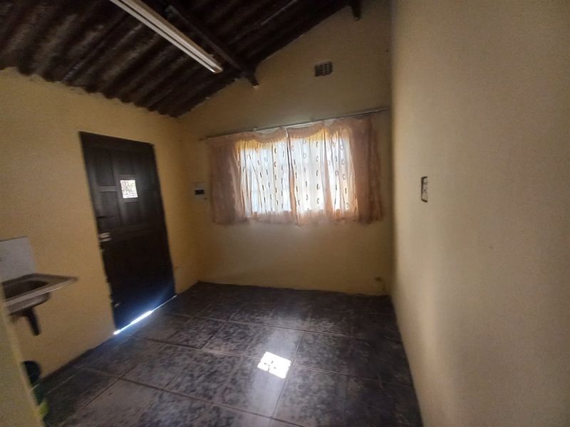 A simple, functional room featuring tiled flooring, exposed roof beams, and a small sink area, suitable for a utility space or basic living area.