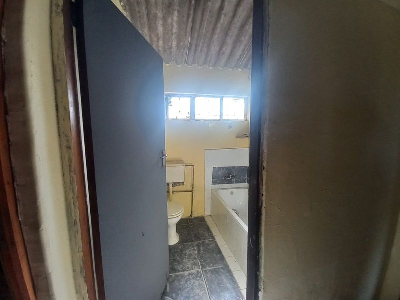A dated bathroom featuring a bathtub, toilet, and basic finishes, requiring significant renovation and cosmetic updates.