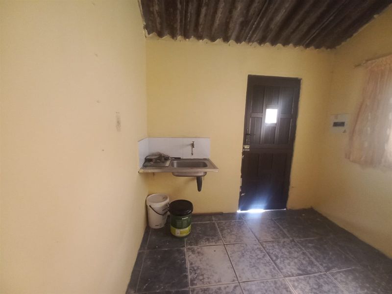 A basic utility or kitchen area featuring a wall-mounted sink, tiled flooring, and direct exterior access through a single door.