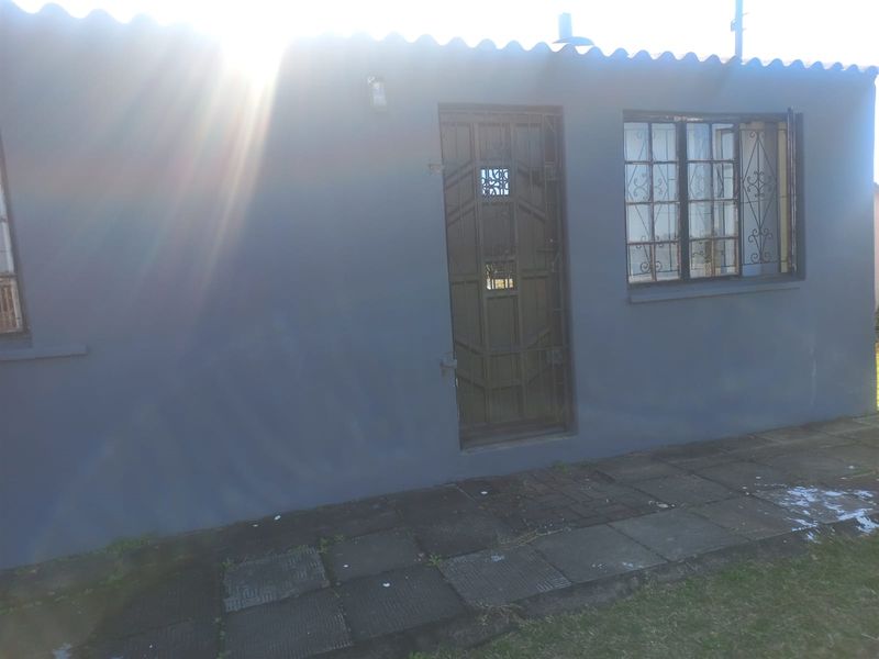 Exterior view of the property featuring a solid door with security gate, metal-framed windows with security bars, and paved walkway.