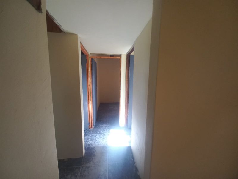 A narrow interior hallway featuring tiled flooring and multiple doorways leading to adjacent rooms.