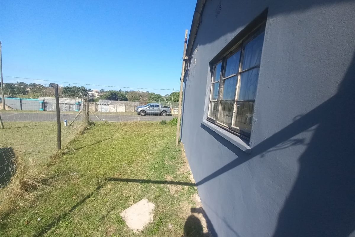 A side view of the property exterior showing the painted wall, metal-framed window, and adjacent grass yard area.