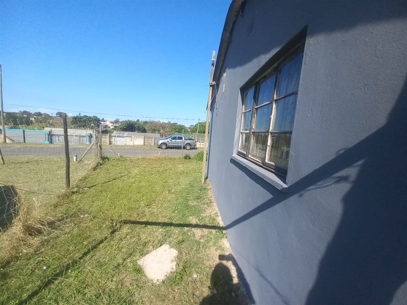 A side view of the property exterior showing the painted wall, metal-framed window, and adjacent grass yard area.