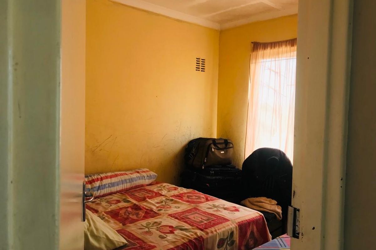 A bedroom featuring yellow walls with visible surface wear and a window with natural light.