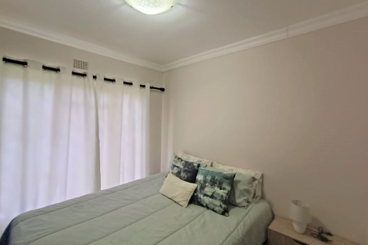 A neutrally painted bedroom featuring classic ceiling cornicing, a central flush mount light fixture, and a curtain rod installed above the window.