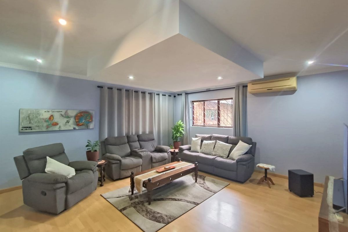 Spacious living room featuring laminate flooring, a recessed ceiling with downlights, and a wall-mounted split-system air conditioner.