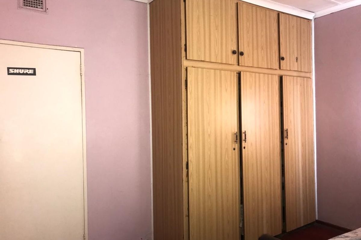 A bedroom featuring a large, dated built-in wooden wardrobe with overhead storage compartments and a ceiling ventilation unit.