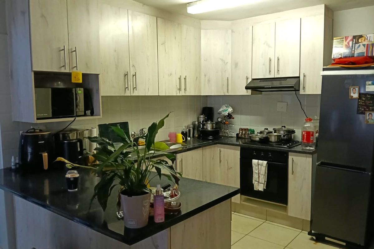 A functional kitchen featuring light wood-grain cabinetry, dark laminate countertops, built-in oven, hob, extractor fan, and tiled flooring.