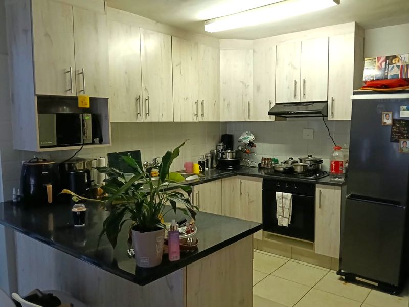 A functional kitchen featuring light wood-grain cabinetry, dark laminate countertops, built-in oven, hob, extractor fan, and tiled flooring.