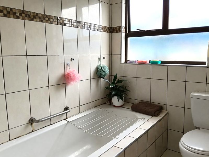 A functional bathroom featuring a built-in bathtub with a grab rail, a standard toilet, and tiled wall finishes throughout.