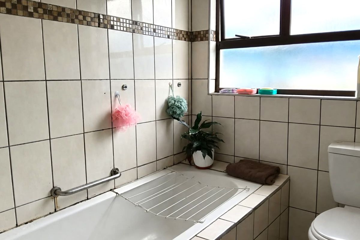 A functional bathroom featuring a built-in bathtub with a grab rail, a standard toilet, and tiled wall finishes throughout.