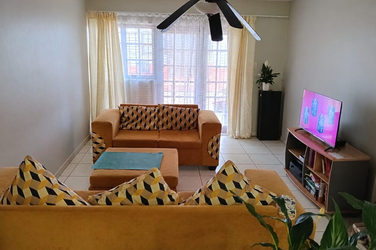 A comfortable living room featuring tiled flooring, a ceiling fan, and a sliding glass door that provides natural light.