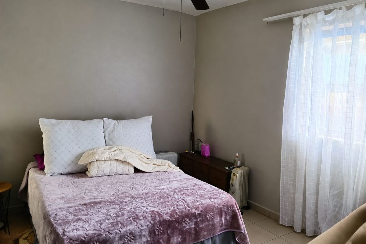 A functional bedroom featuring tiled flooring, a ceiling fan, and natural light through a window with installed curtain rods.