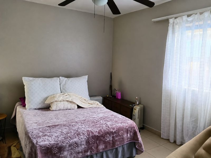 A functional bedroom featuring tiled flooring, a ceiling fan, and natural light through a window with installed curtain rods.